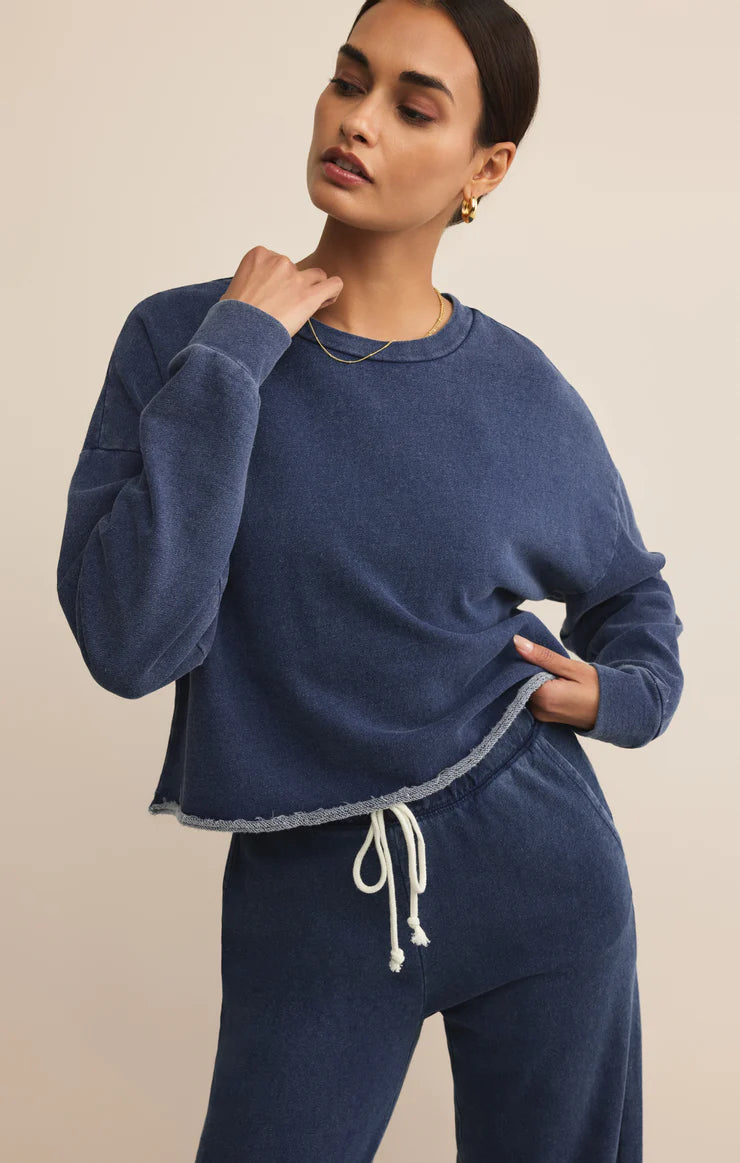 Woman with dark hair wearing a blue knit denim sweatshirt and matching pants standing against a beige background
