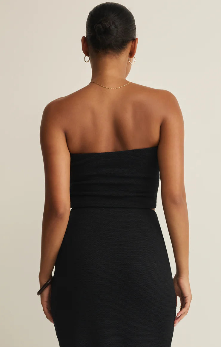 Back view of woman wearing black Z Supply Caffari Tube Top Tank styled with a matching high-waisted skirt in boutique setting