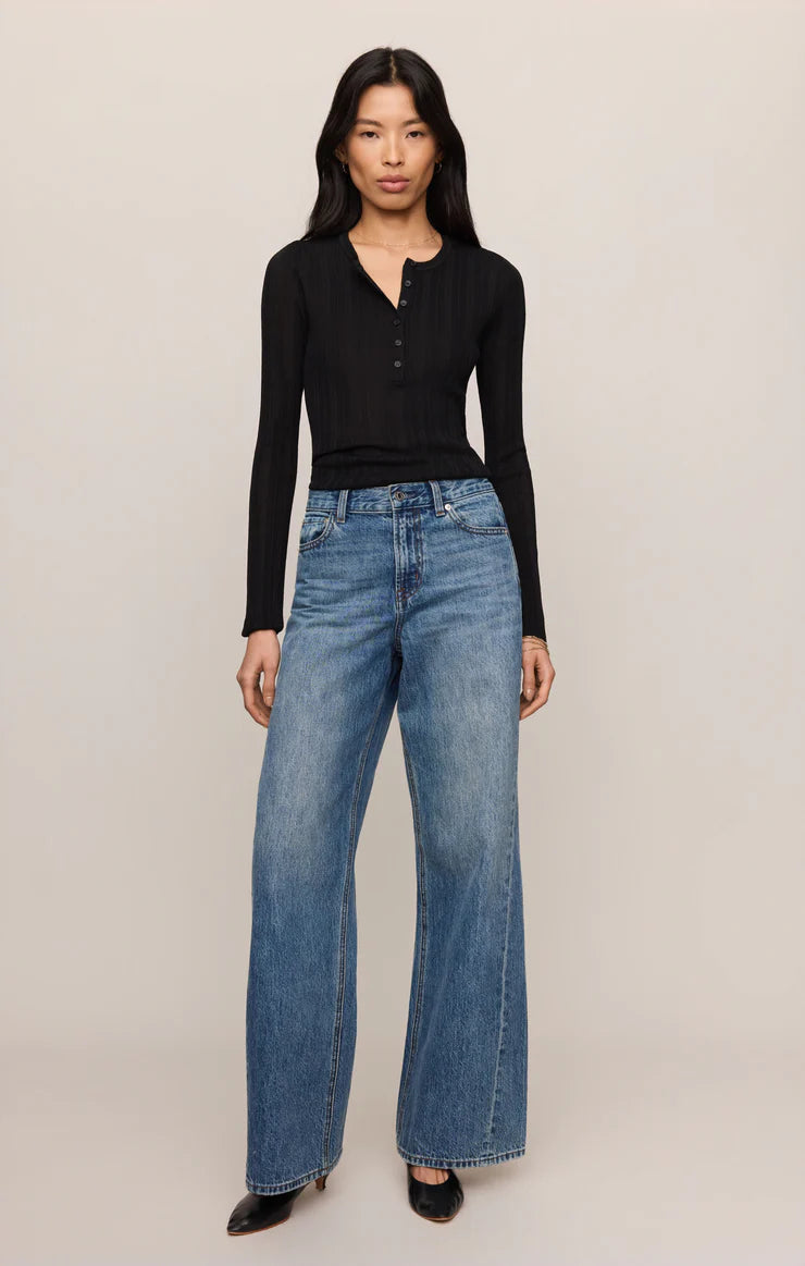 Model wearing a black Rowena Fine Knit Sweater by z supply paired with blue wide-leg jeans and black shoes.