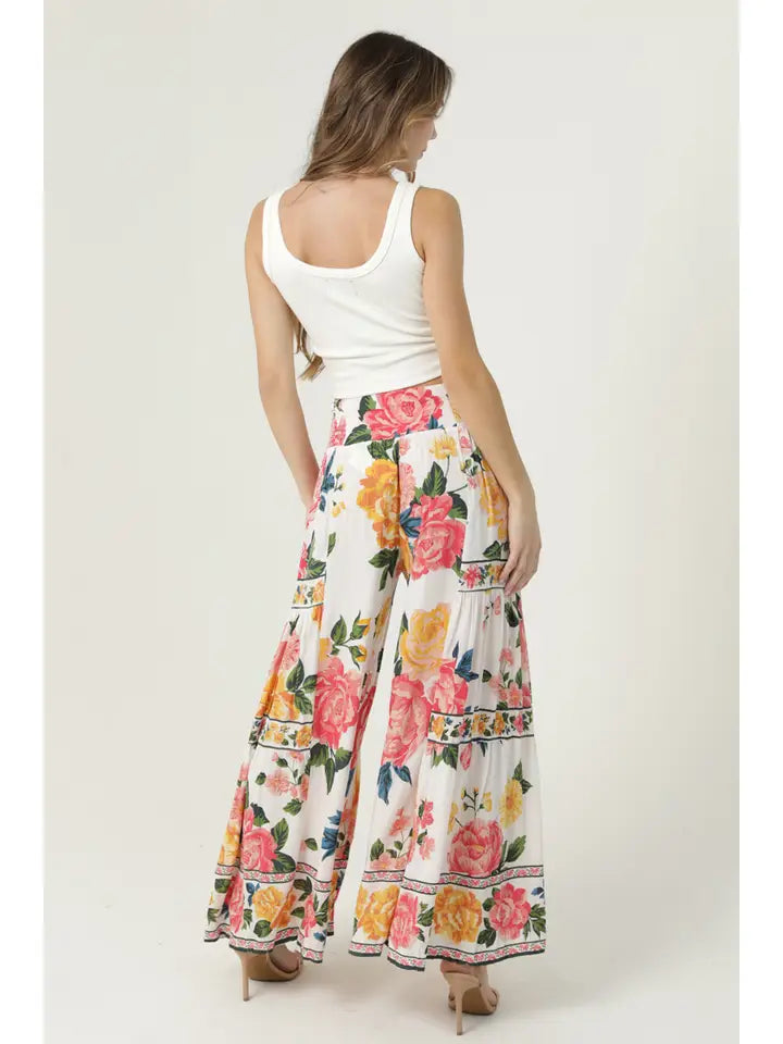 Woman wearing angie Floral Wide Leg Pants with colorful rose pattern and white tank top, viewed from the back