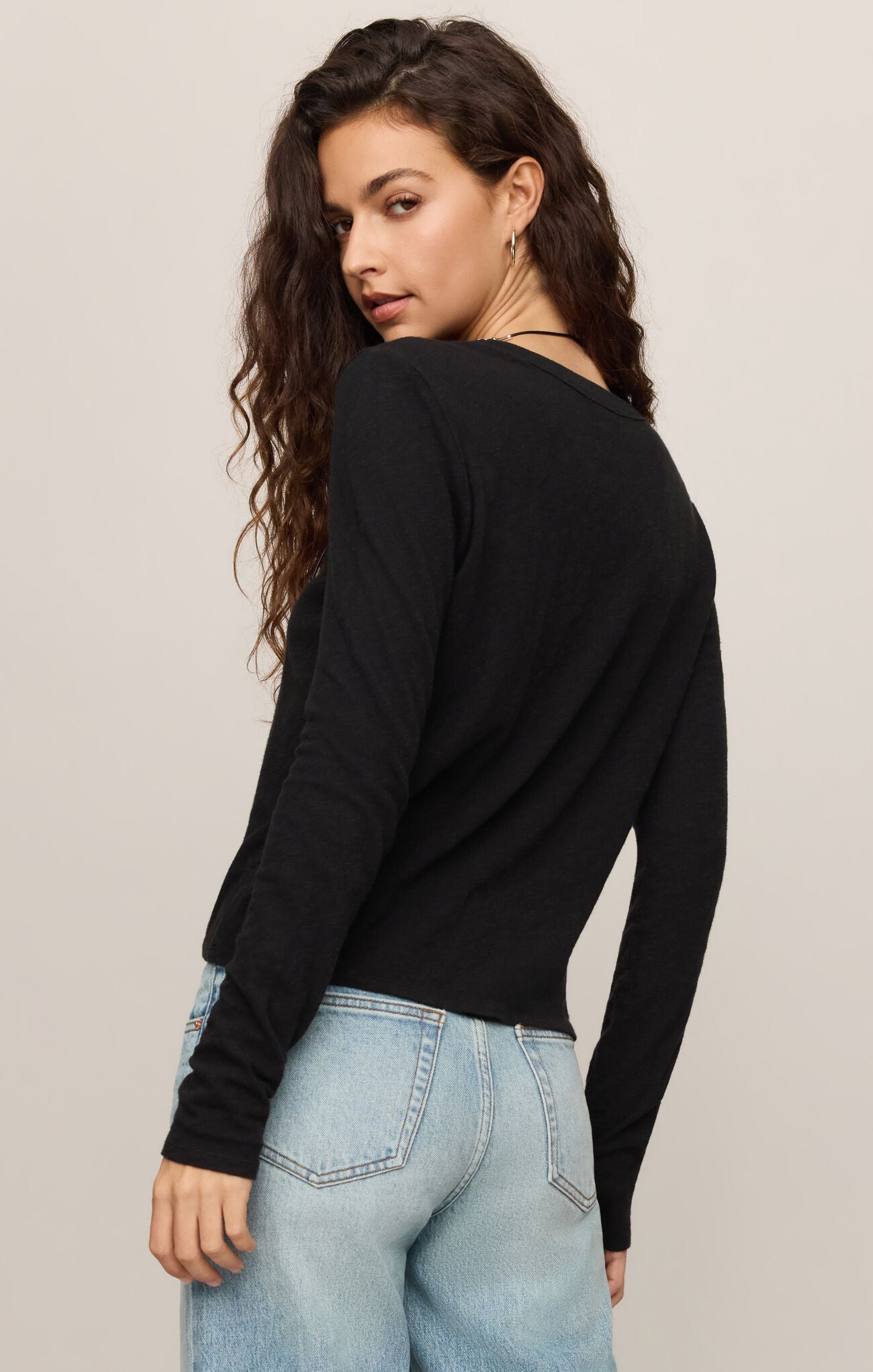 Woman wearing black Junie Long Sleeve Tee by z supply with light blue jeans, posing with back turned and head over shoulder