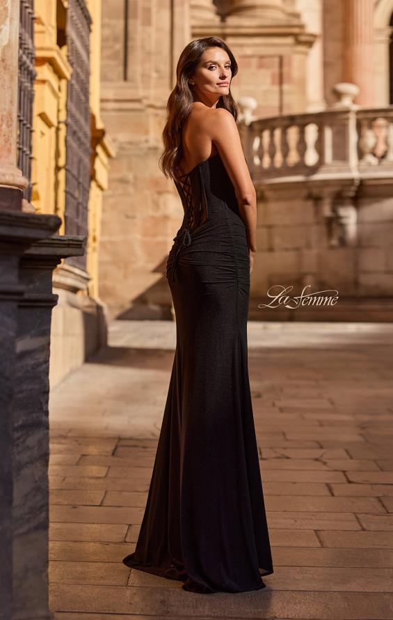 Woman wearing black La Femme Prom Dress Style 33199 with lace-up back standing outdoors near stone railing