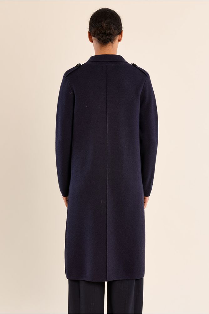 Back view of a person wearing a long dark navy coat with shoulder details and matching trousers