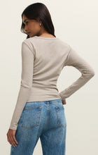 Woman with long dark hair wearing a natural heather fitted long sleeve crew neck top and light blue jeans facing away