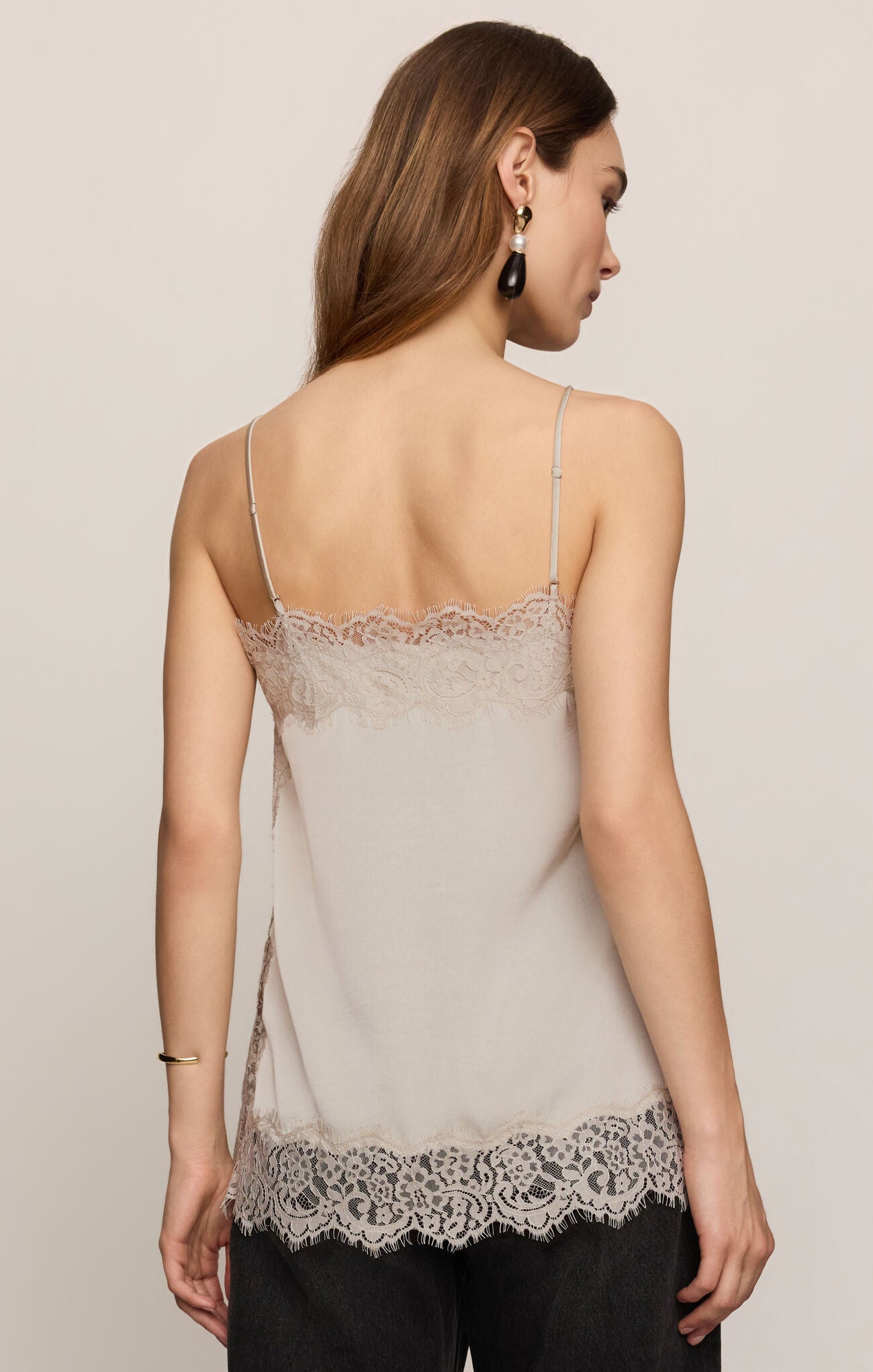 Woman viewed from behind wearing a beige lace trimmed camisole and black pants