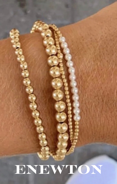 Gold and pearl beaded bracelets on a wrist with 'ENEWTON' branding.