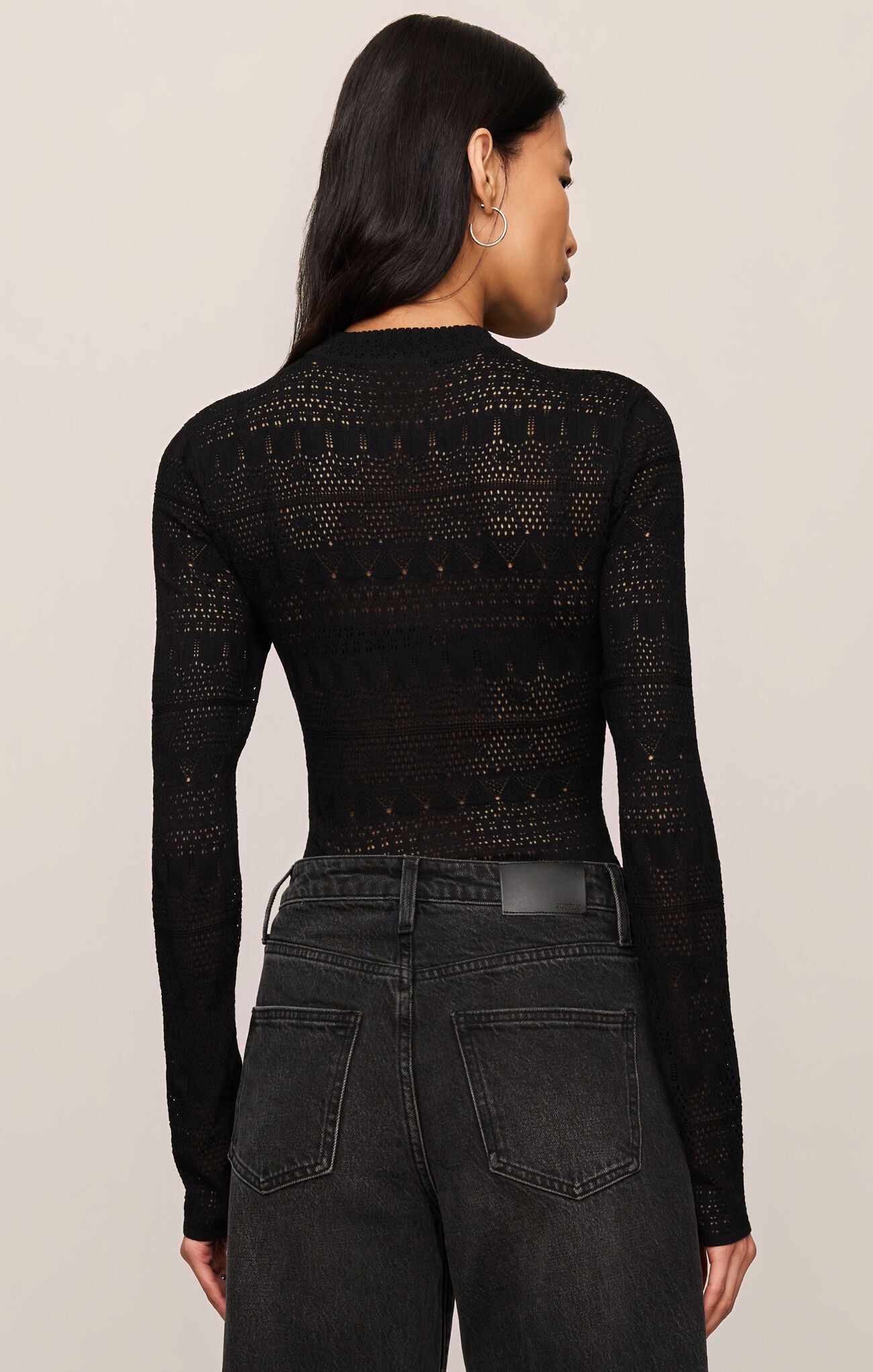 Rear view of woman wearing Black Avery Sweater Top by z supply with intricate knit design and black denim jeans