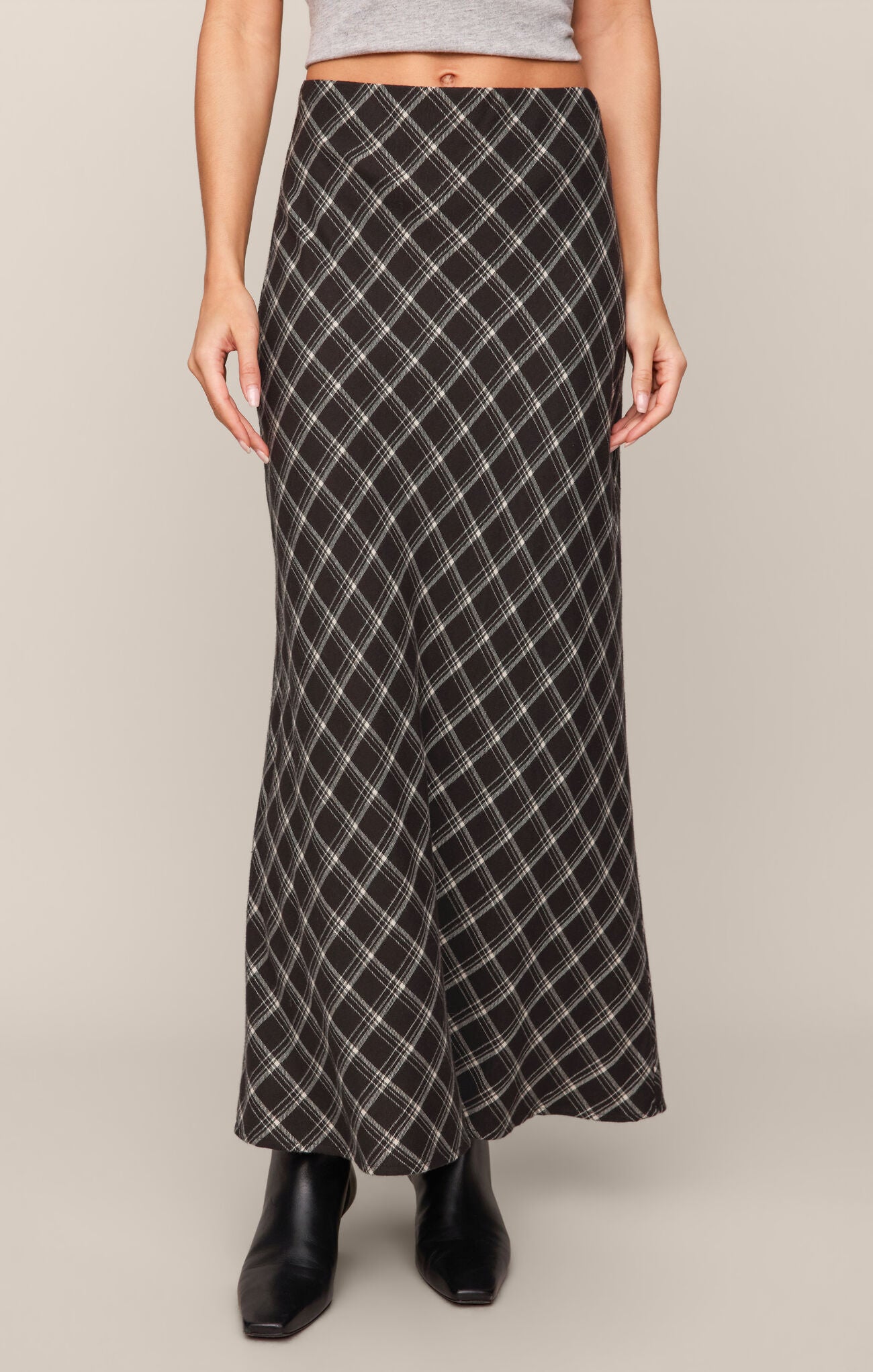Front view of a model wearing Ash Black Europa Plaid Skirt by z supply paired with black ankle boots.