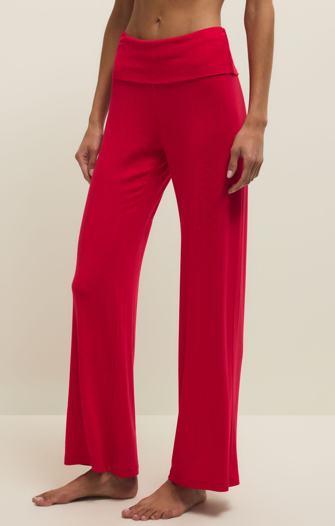 Woman wearing vibrant red fold-over waistband wide-leg pants standing barefoot against a beige background