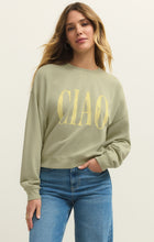 Woman with long blonde hair wearing a sage green sweatshirt with yellow 
