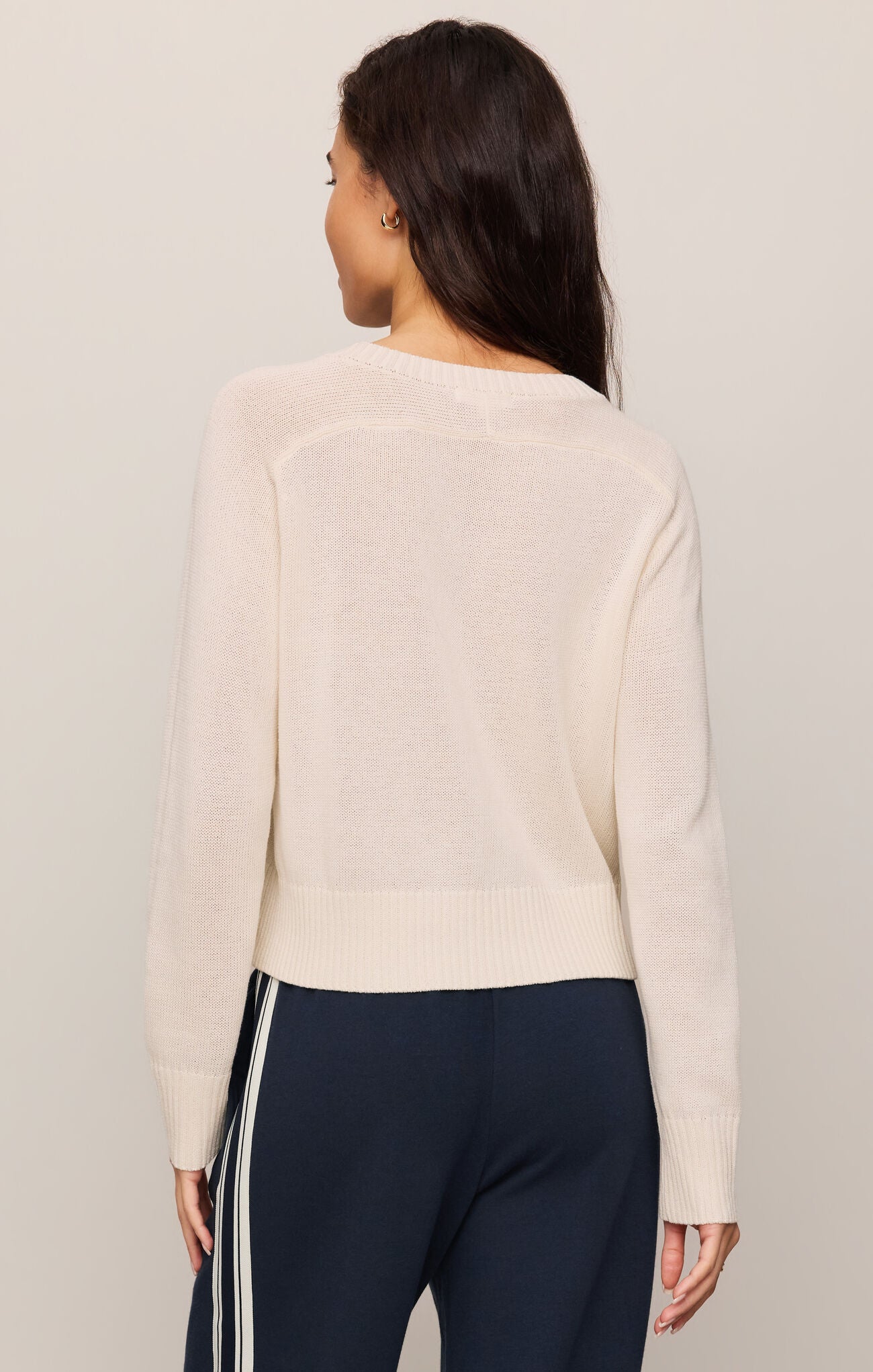 Woman wearing a Sandstone Varsity Stand in Sweater by z supply, shown from the back with navy striped pants