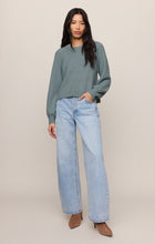 Woman wearing a Soft Succulent Coming Up Sweater by z supply in muted green with light blue wide-leg jeans and brown heels