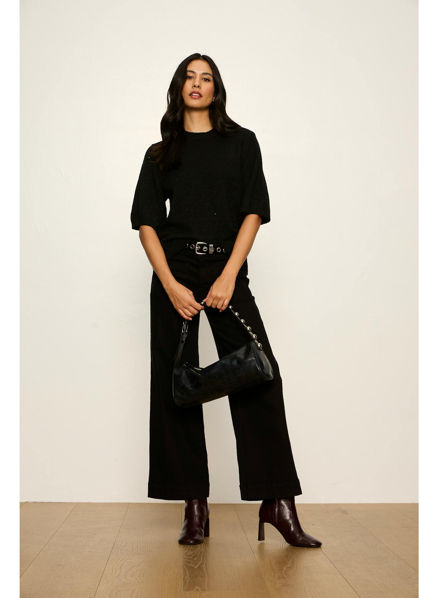 Woman wearing Black Perfect Sequin Sweater Tee by Sanctuary paired with black pants and ankle boots, holding a black bag.