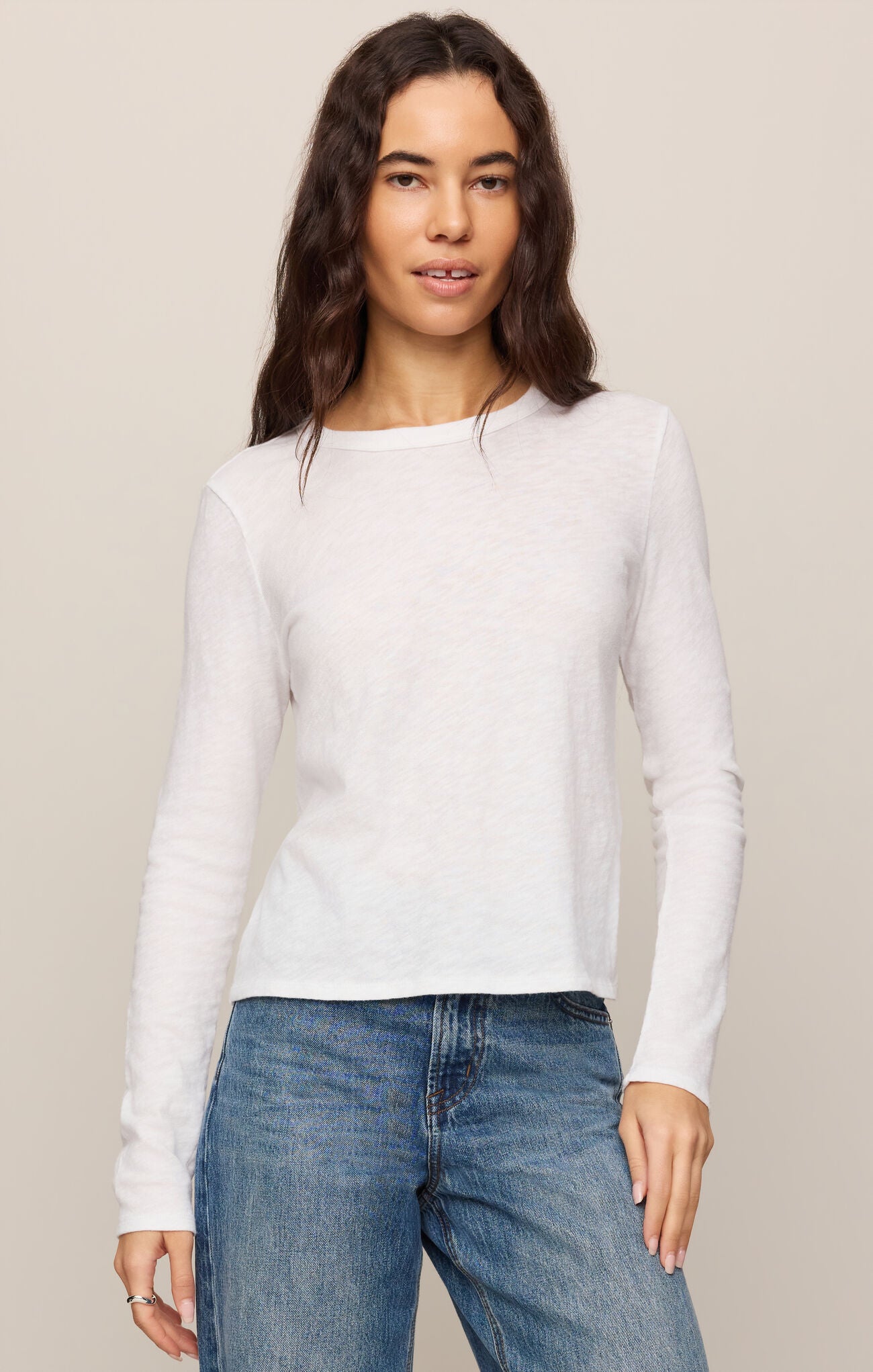Woman wearing a white Junie Long Sleeve Tee by z supply paired with blue jeans against a neutral background