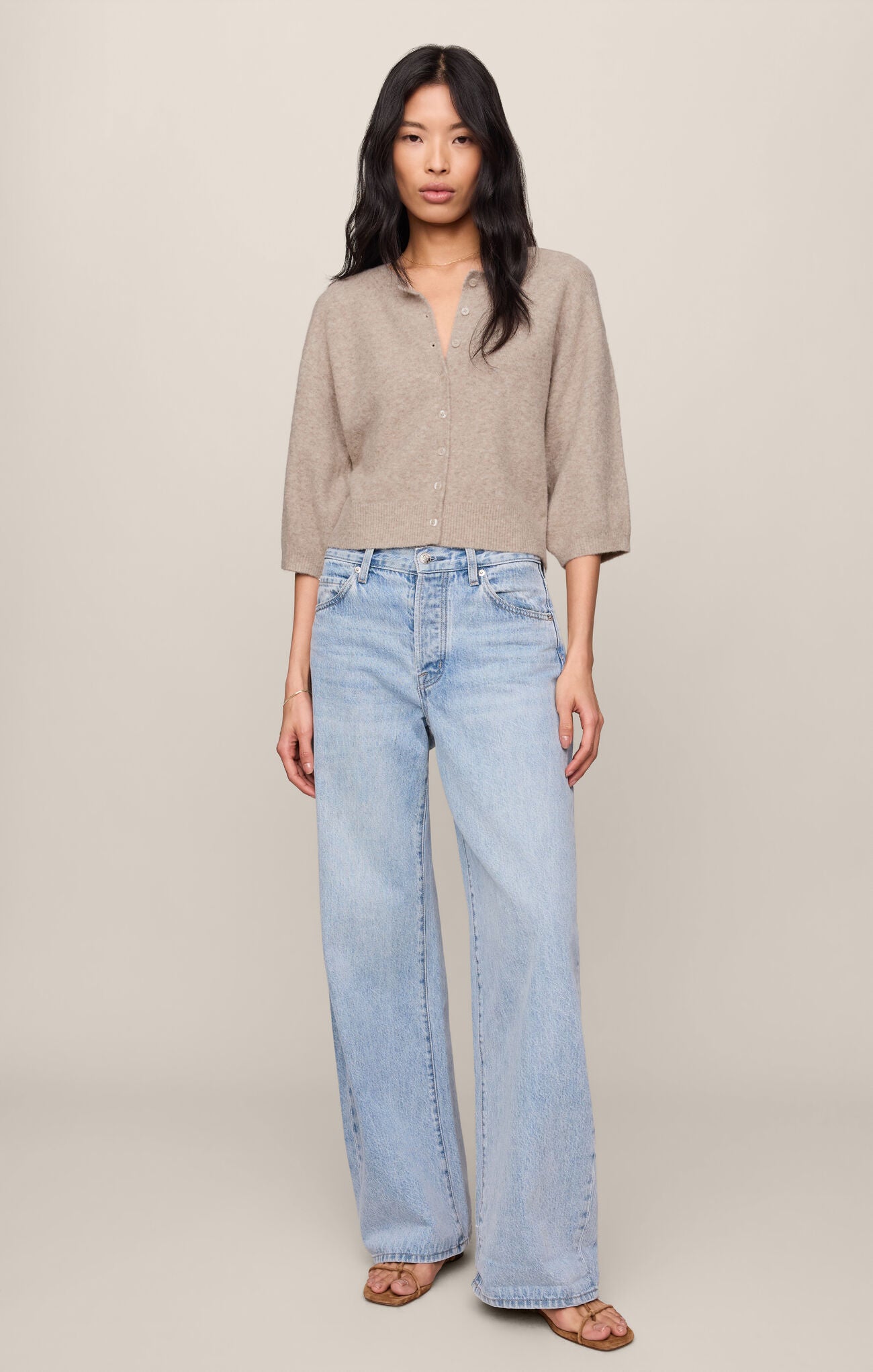 Woman wearing a Natural Heather Valor Cardigan by z supply with light wash wide-leg jeans and sandals standing against beige background
