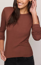 Smiling woman wearing a fitted brown long sleeve shirt and black jeans