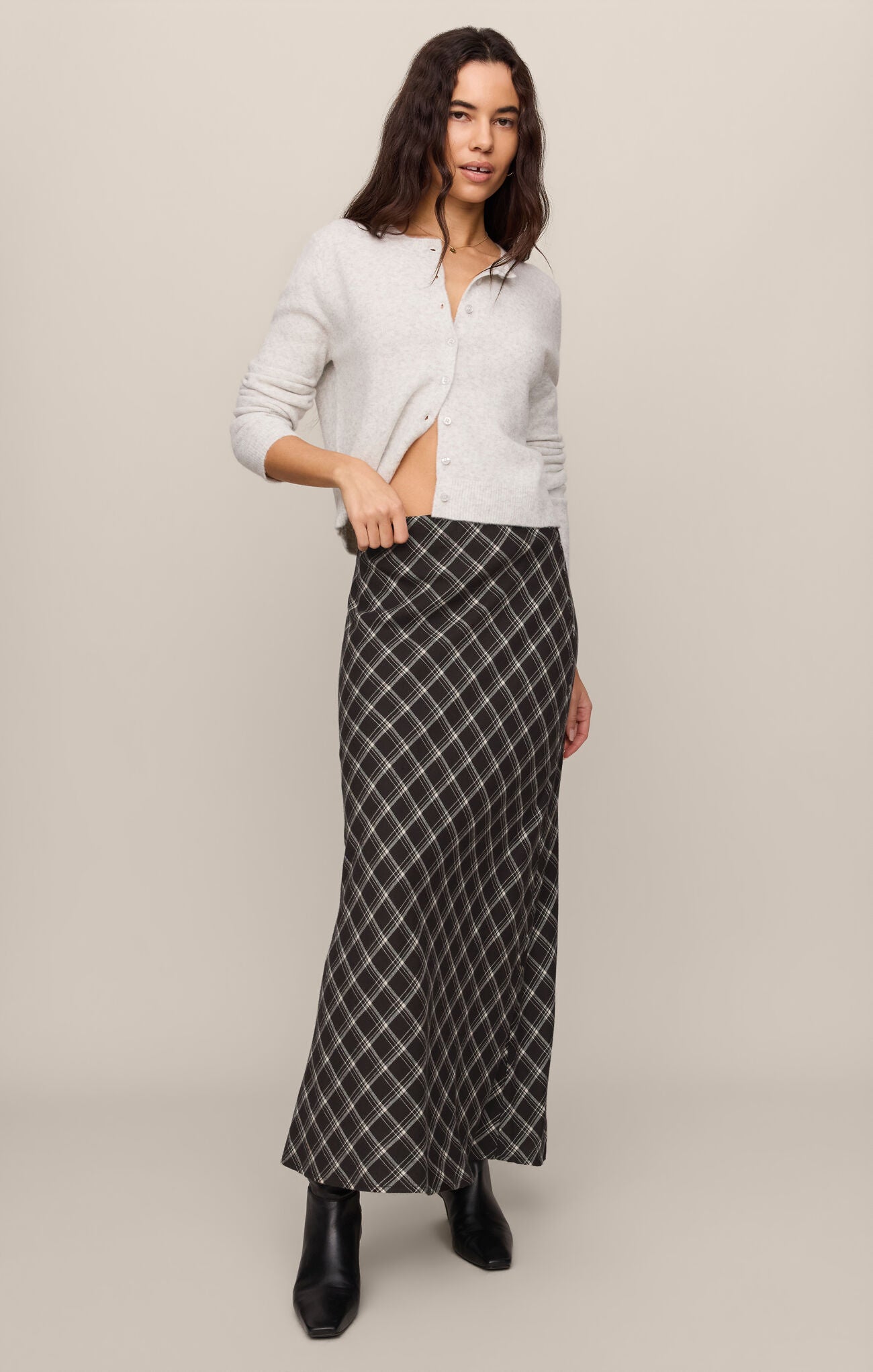 Woman wearing a white cardigan paired with an Ash Black Europa Plaid Skirt by z supply and black boots