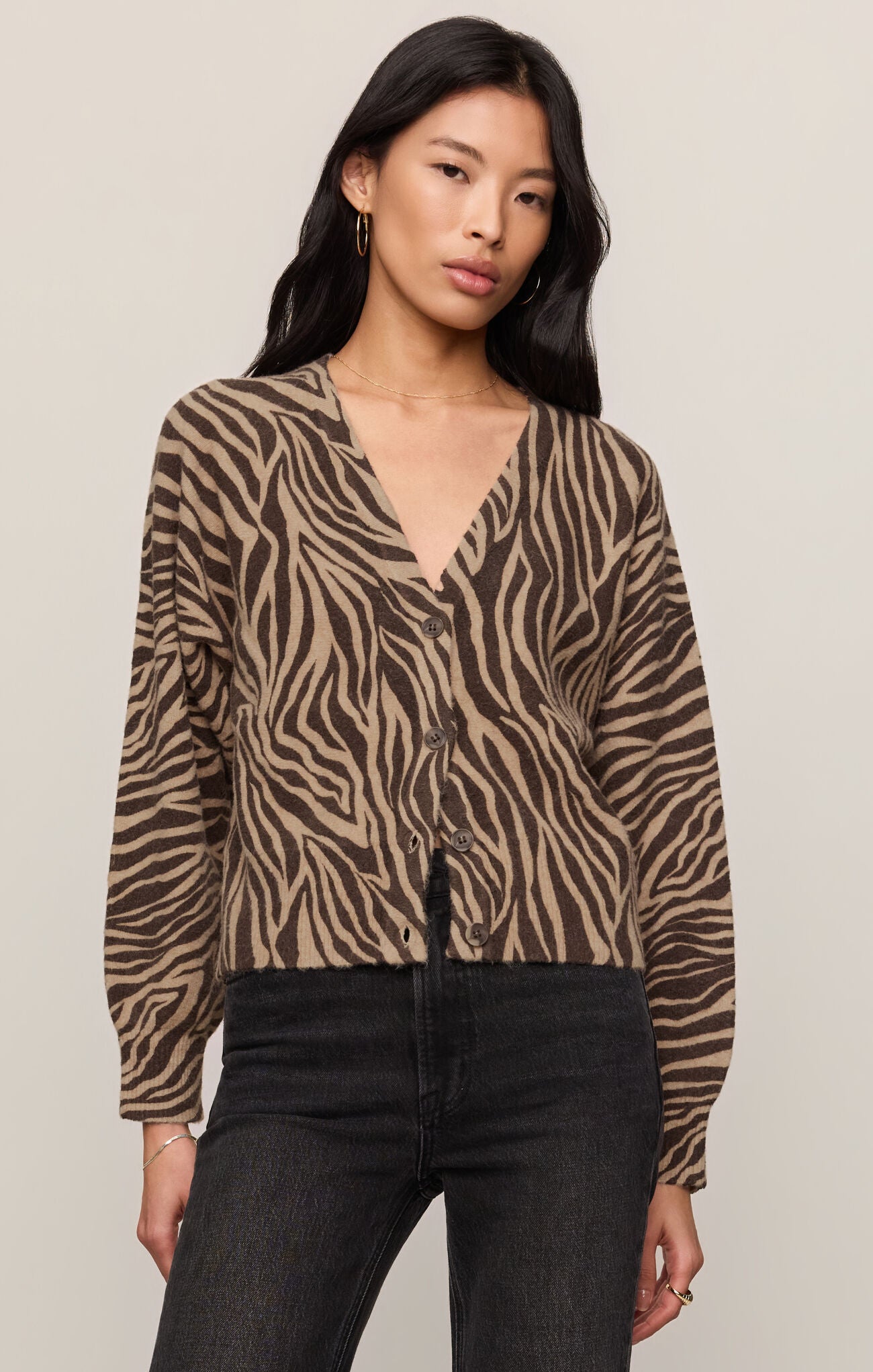 Woman wearing a zebra print Dark Chocolate All The Wild Cardigan by z supply with black jeans against beige background