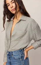 Woman wearing an Emerald Cove River Plaid Button Up by z supply paired with high-waisted blue jeans against neutral background