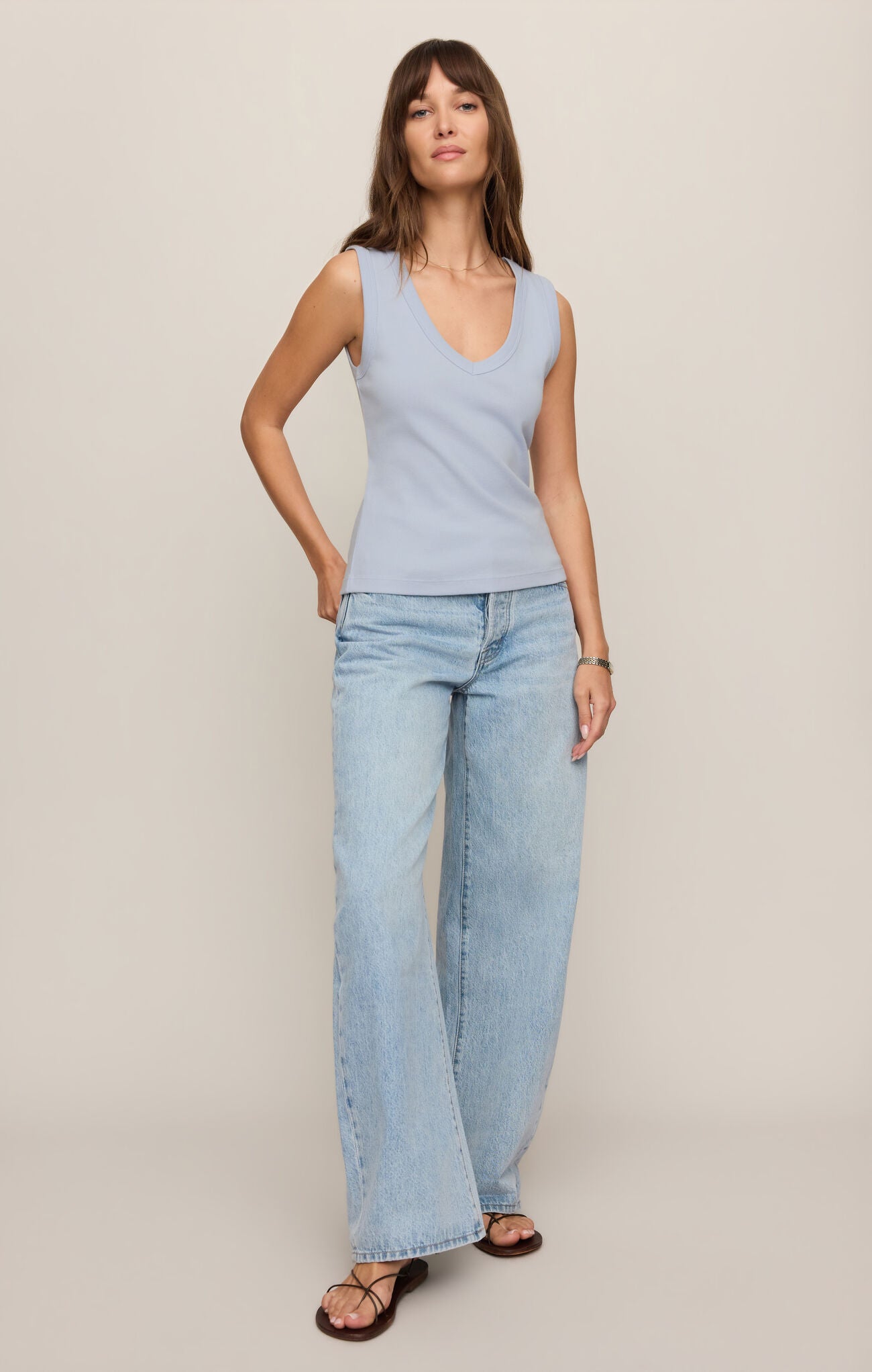 Woman wearing a light blue Skyline Ellie V Neck Tank by z supply paired with wide-leg jeans and sandals standing against a neutral wall