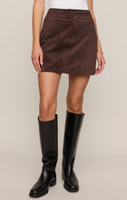 Woman wearing Dark Chocolate Perri Suede Mini Skirt and black knee-high boots by z supply against beige background