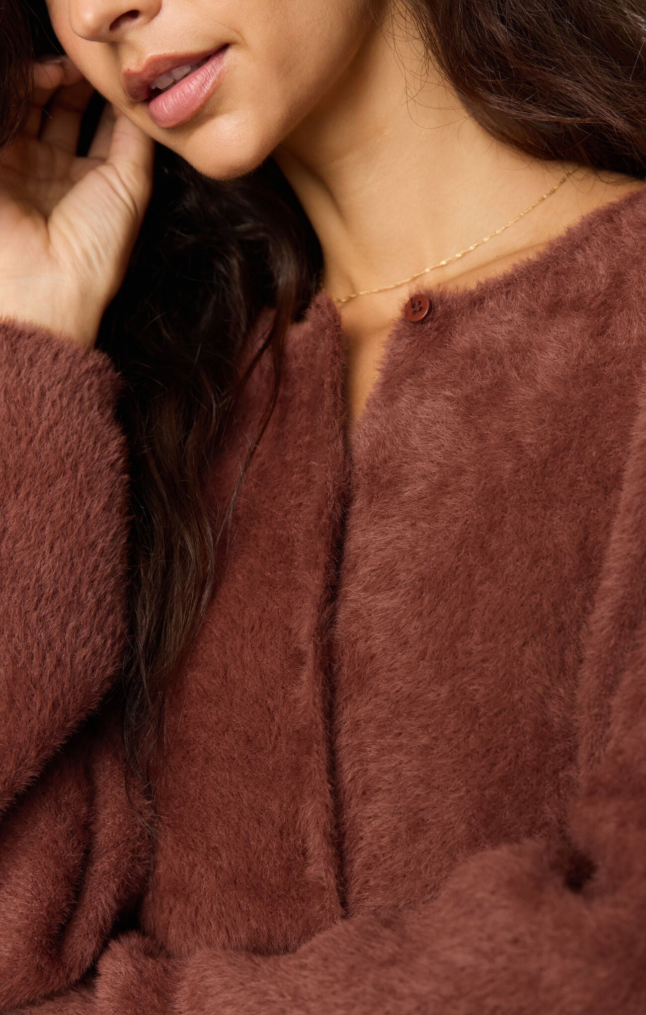 Close-up portrait of a woman in a soft brown textured sweater wearing a delicate gold necklace