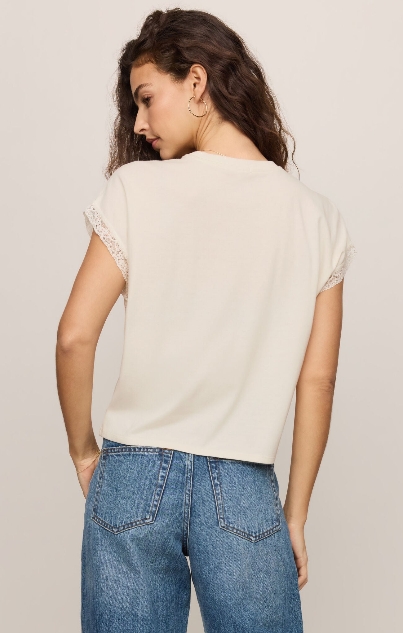 Woman wearing an off-white Cloud Marika Lace Trim Muscle Tee by z supply with lace details on sleeve edges shown from back