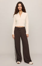 Woman wearing a cream Sandstone Summit Half Zip Sweater by z supply with long sleeves and a zip collar standing against beige background.