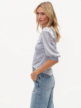 Woman wearing six/fifty Denim Solara Mixed Media Satin SS Top with puff sleeves paired with light blue jeans against white background