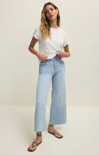 Woman with long blonde hair wearing a white t-shirt and light blue high-rise wide-leg cropped jeans with strappy sandals