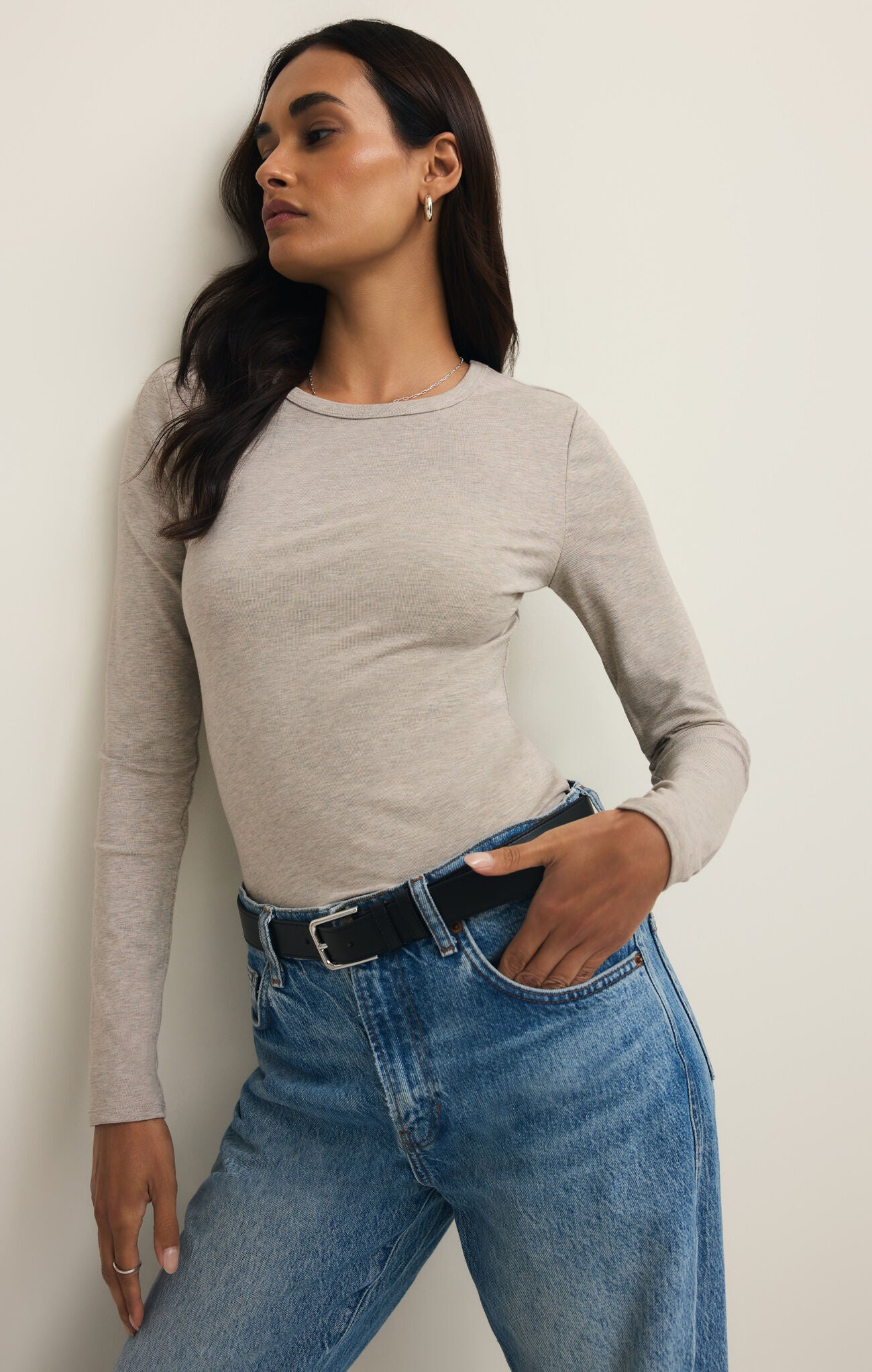 Woman with dark hair wearing a natural heather long sleeve crew neck top tucked into high-rise blue jeans