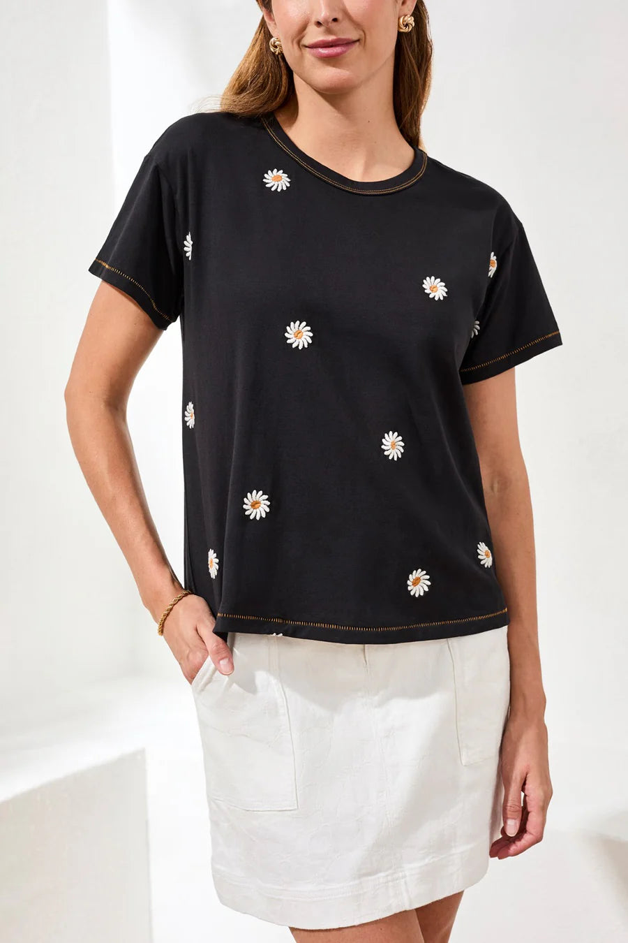 Woman wearing Tribal Embroidered Daisy Short Sleeve Crew Neck Top in black paired with a white skirt in a bright setting