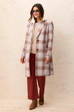 Woman in sunglasses wearing a long plaid coat beige sweater burgundy pants and brown ankle boots