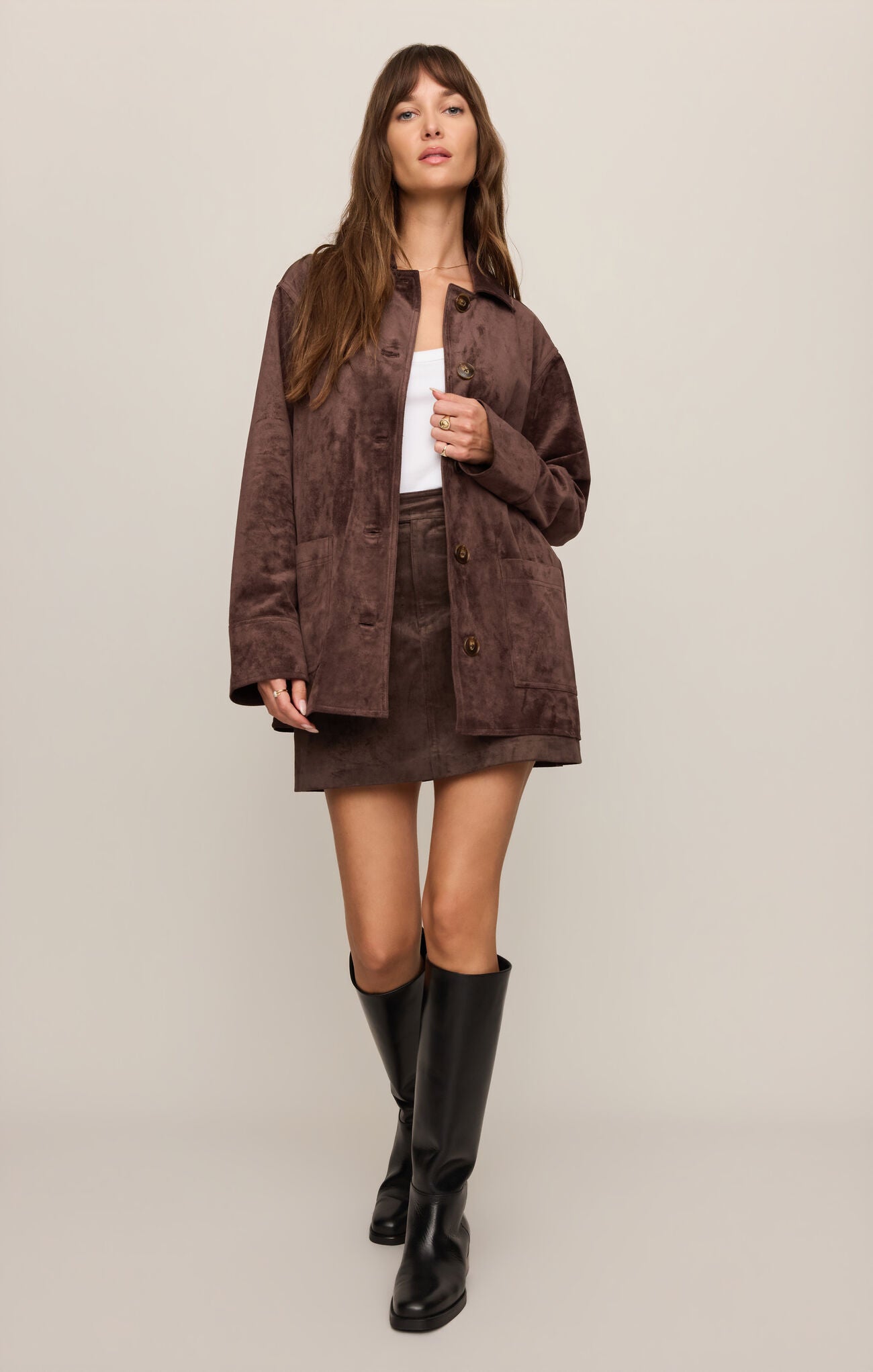 Woman wearing a Dark Chocolate Perri Suede Mini Skirt and matching jacket by z supply with black knee-high boots.