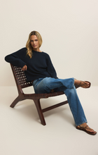 Woman seated on wooden chair wearing z supply Eclipse Bellami Sweater in navy paired with blue jeans and sandals