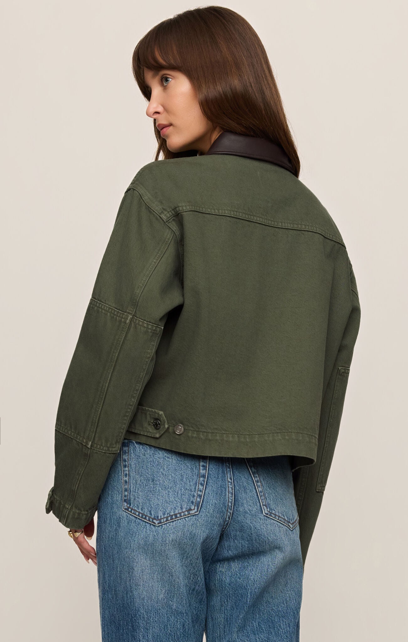 Woman wearing a green Dusk Sage Rey Cropped Chore Jacket by z supply, shown from the back with denim jeans