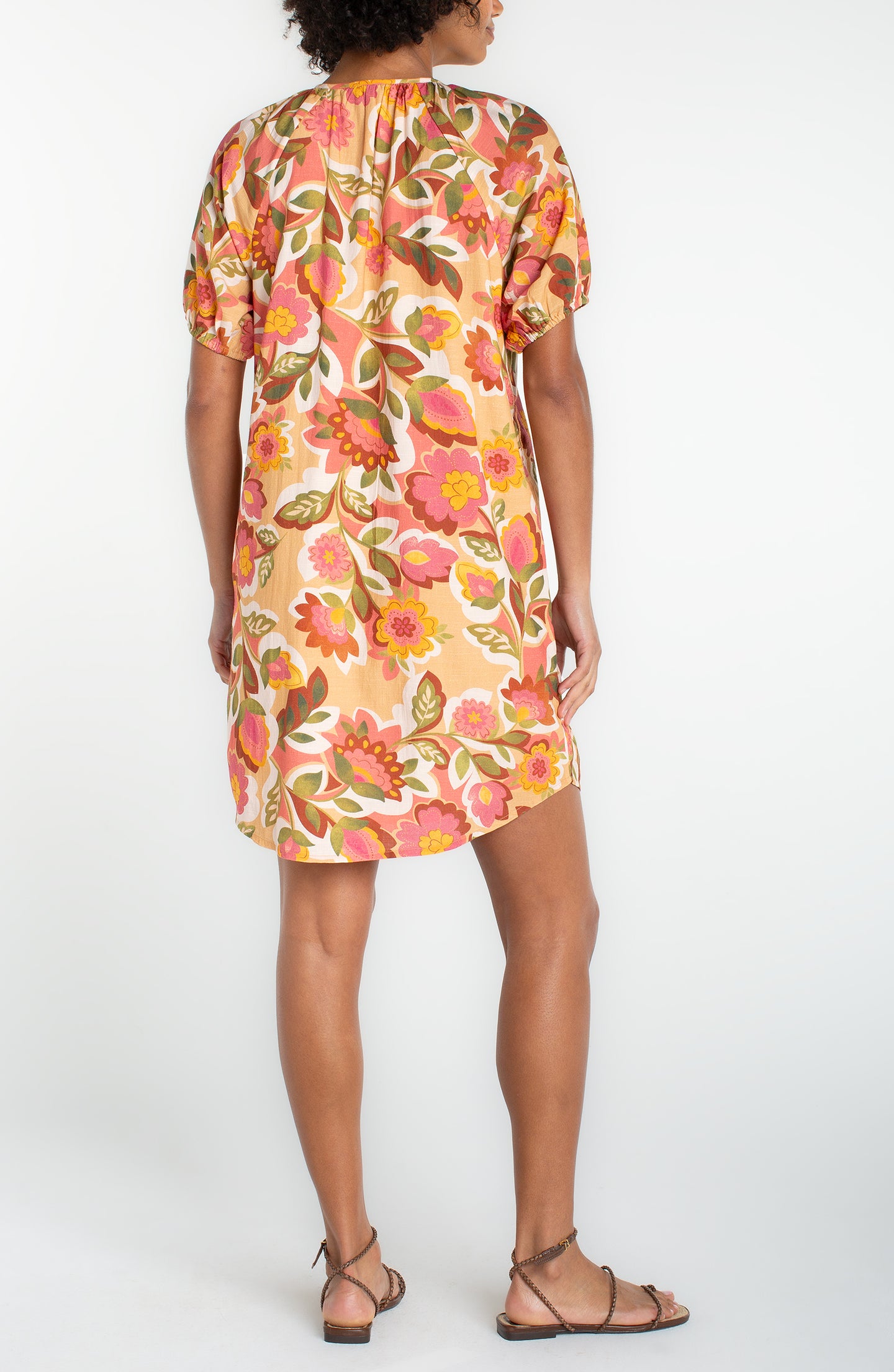 Back view of a woman wearing a tan floral short sleeve shirred button front woven dress by liverpool