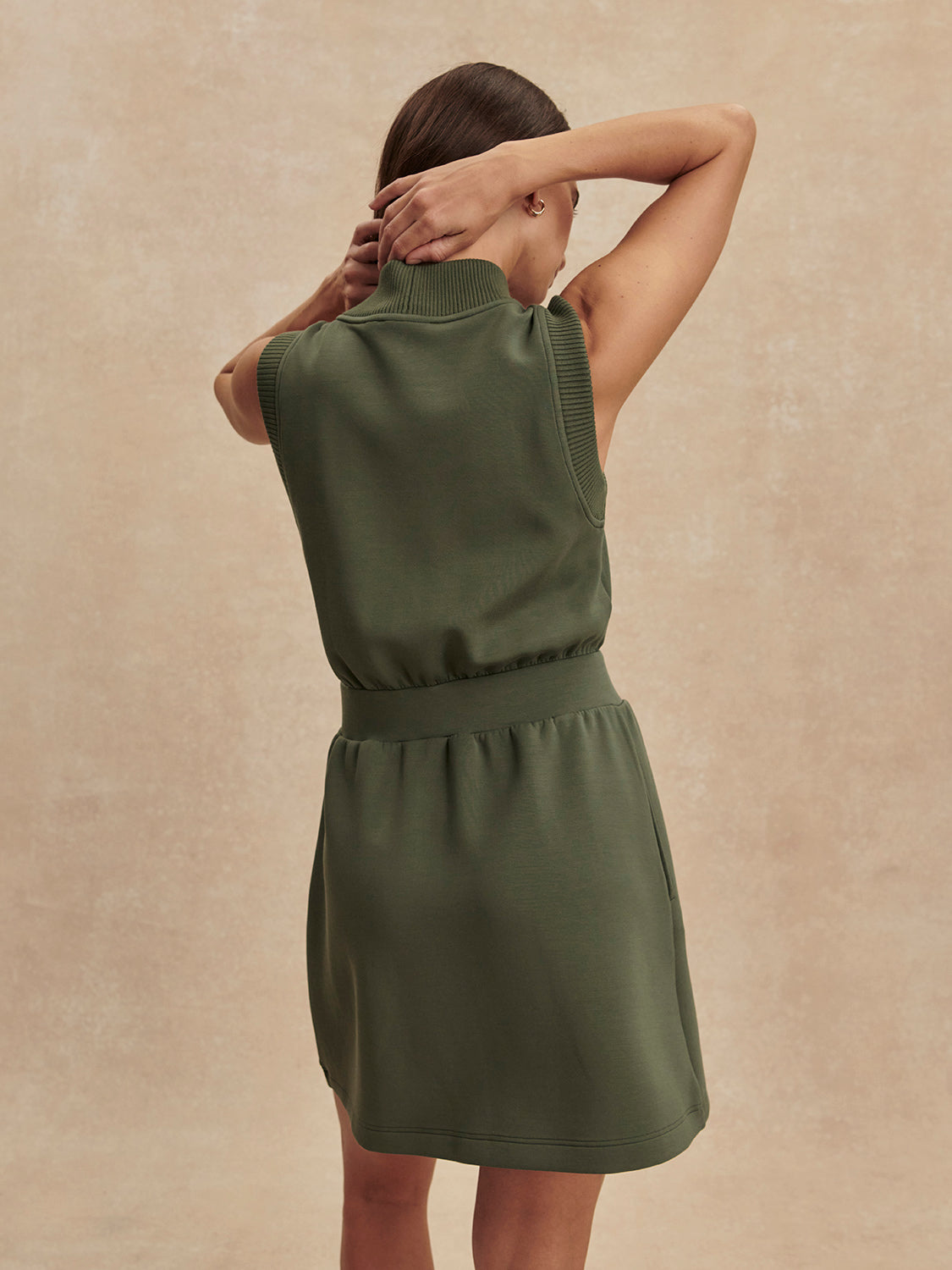 Woman seen from behind wearing an olive green Thyme Polyanna Half Zip Dress by Varley with sleeveless design and high collar.