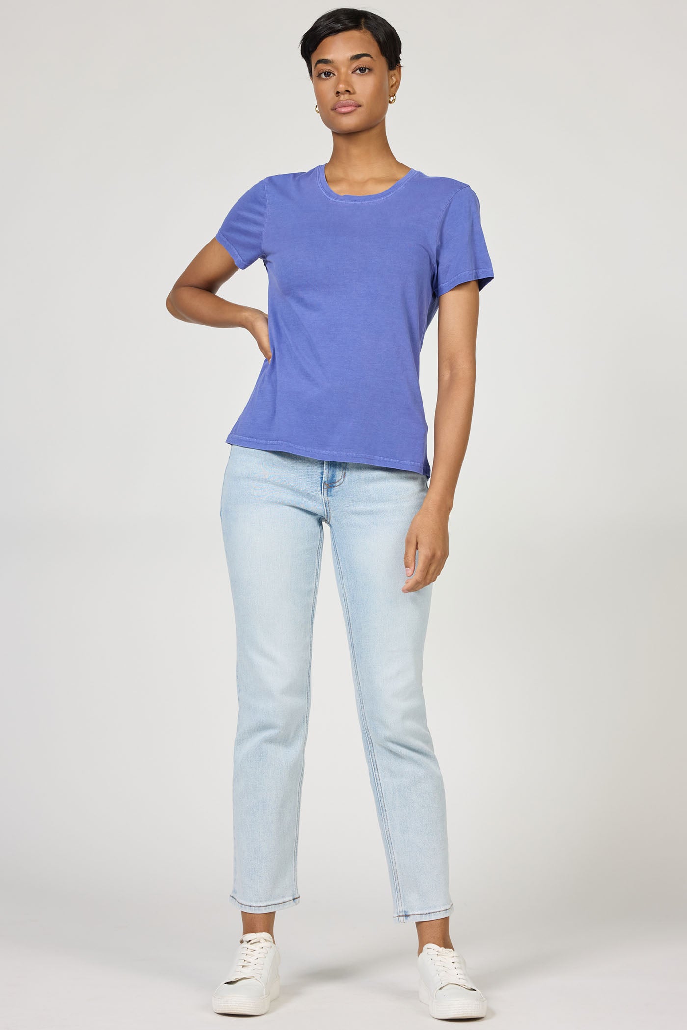 Model wearing dear john Pigment Skipper Blue Unity Tee paired with light denim jeans and white sneakers in studio setting