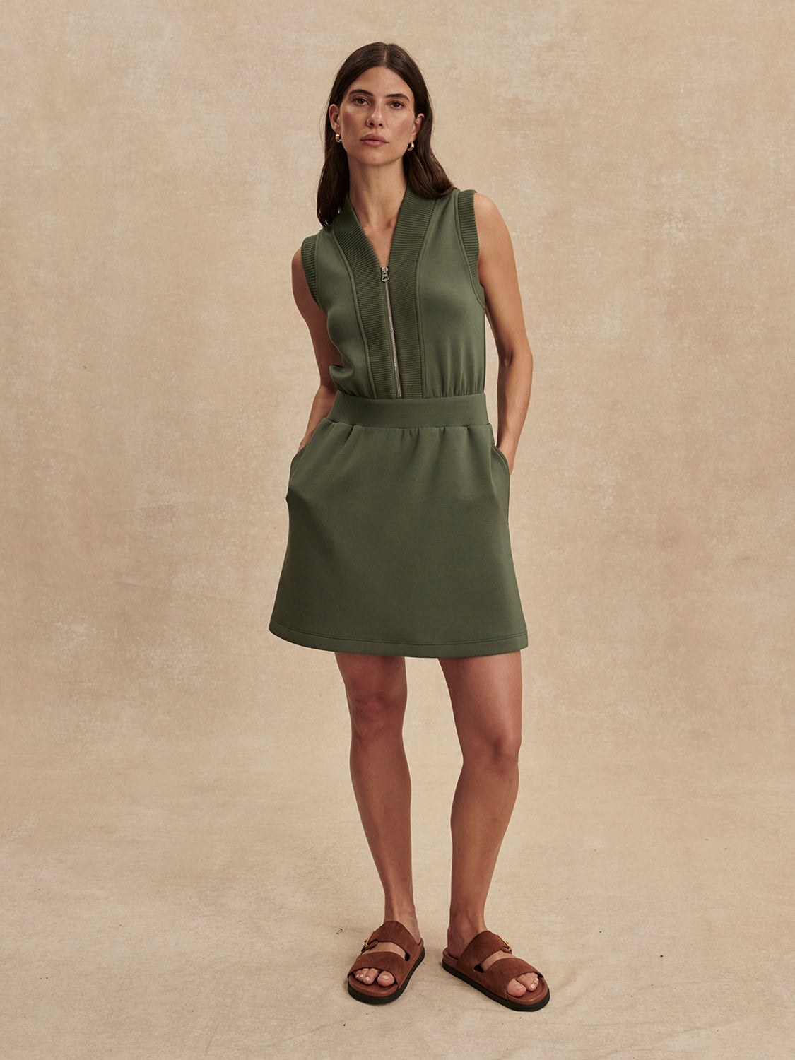 Woman wearing olive green sleeveless Thyme Polyanna Half Zip Dress by Varley with zip front and side pockets