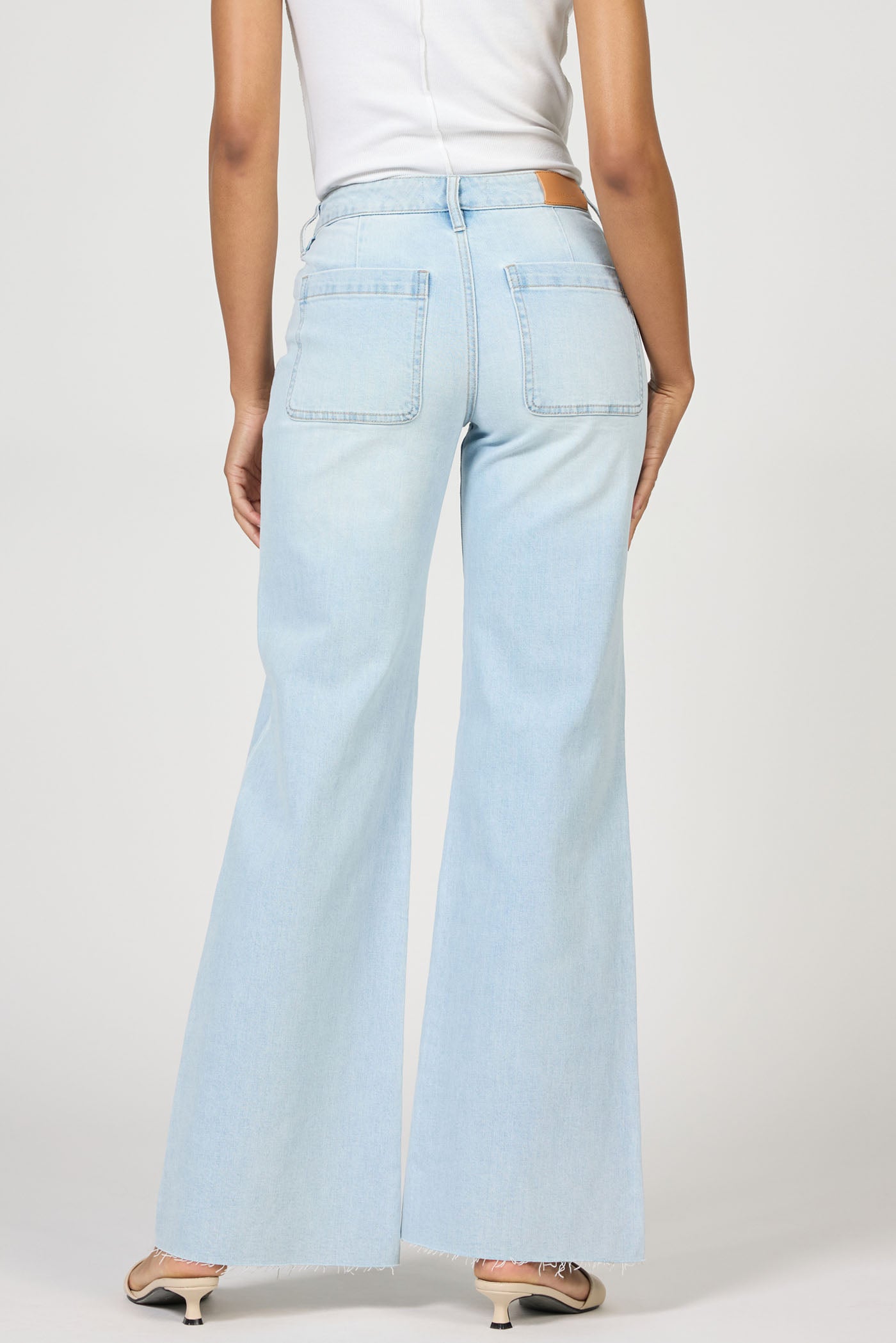 Rear view of a model wearing light wash Misty Cloud Micah Jeans by dear john with a flared leg and raw hem details