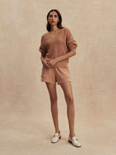 Woman wearing a camel-colored Camel Gaia V Neck Sweater by Varley paired with matching shorts in a neutral background.