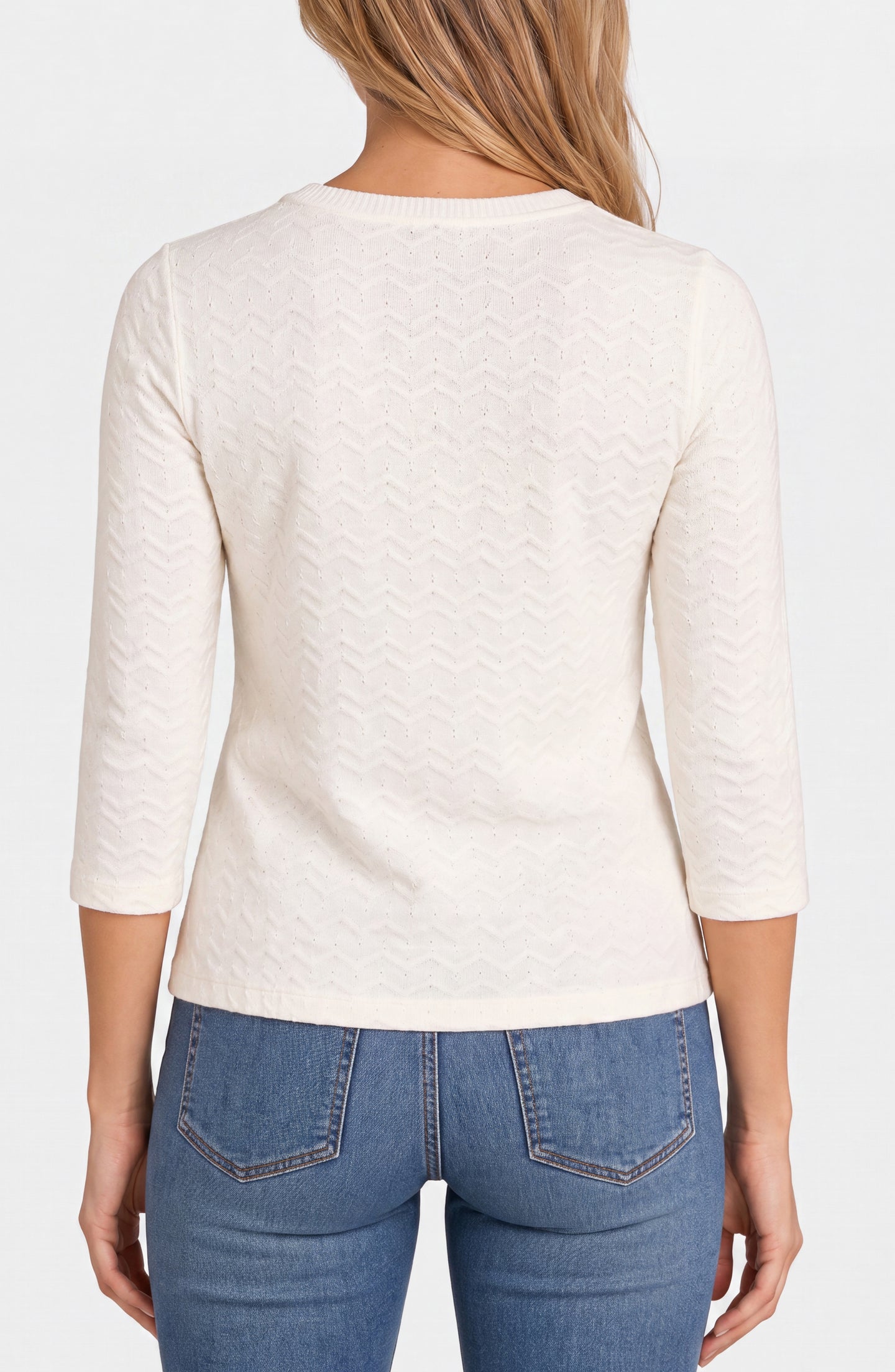 Woman wearing a white textured long sleeve top and blue denim jeans shown from the back on a plain background.