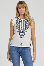 Woman wearing Egret Nicola Tank by dear john with blue floral embroidery and ruffle shoulders paired with jeans