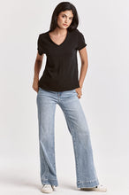 Woman wearing a black Vanya V Neck Tee by dear john paired with light blue jeans and white sneakers against a plain background