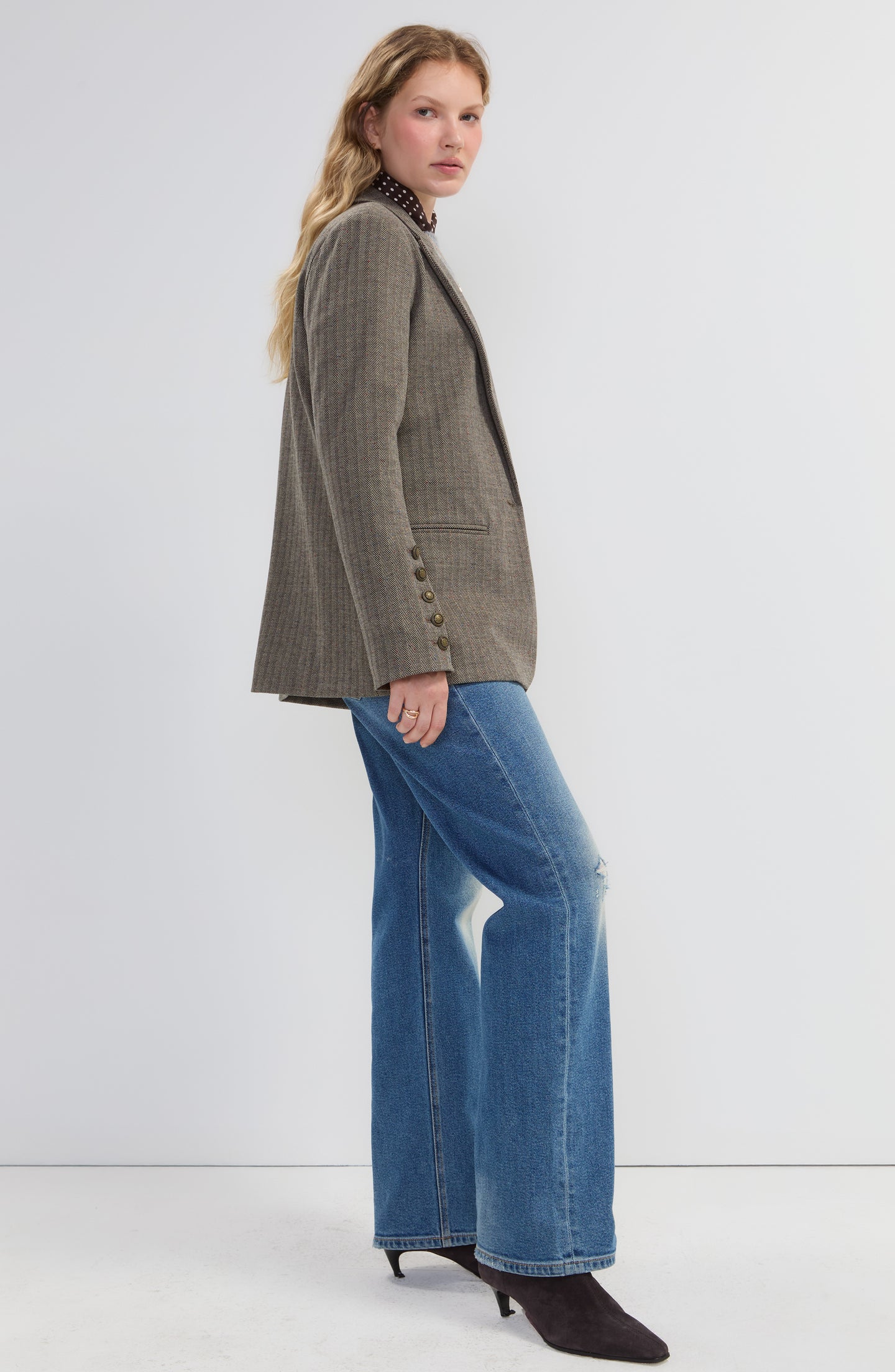 Side view of a woman wearing a Brown Blazer with Button Sleeve by liverpool paired with blue jeans and black heels