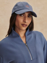 Woman wearing a Varley Bijou Blue Davidson Sweat with a zip collar and matching blue cap against beige background