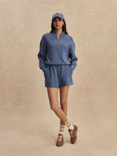 Woman wearing Varley Bijou Blue Davidson Sweat with matching shorts and cap, styled with sneakers and socks.