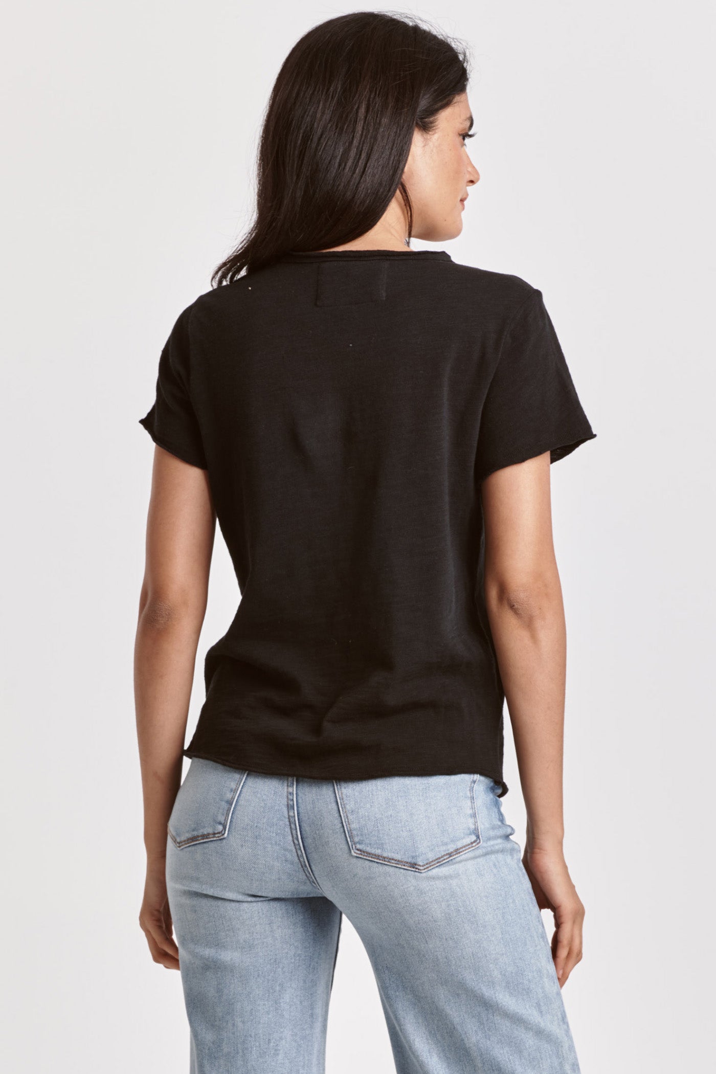Woman wearing black Vanya V Neck Tee by dear john shown from the back with light blue jeans against white background