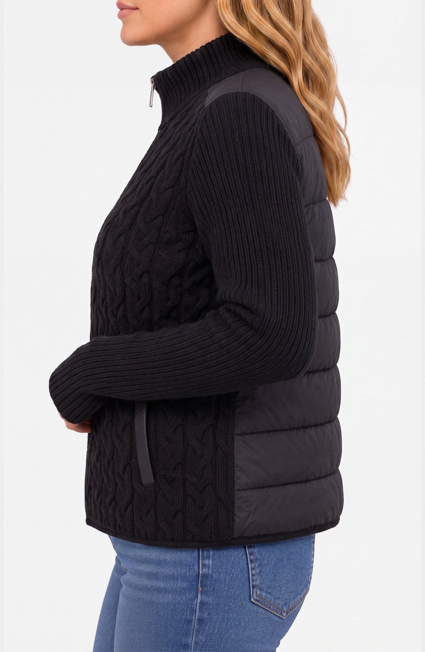 Side view of a woman wearing a black knitted and quilted jacket with a high collar and blue jeans